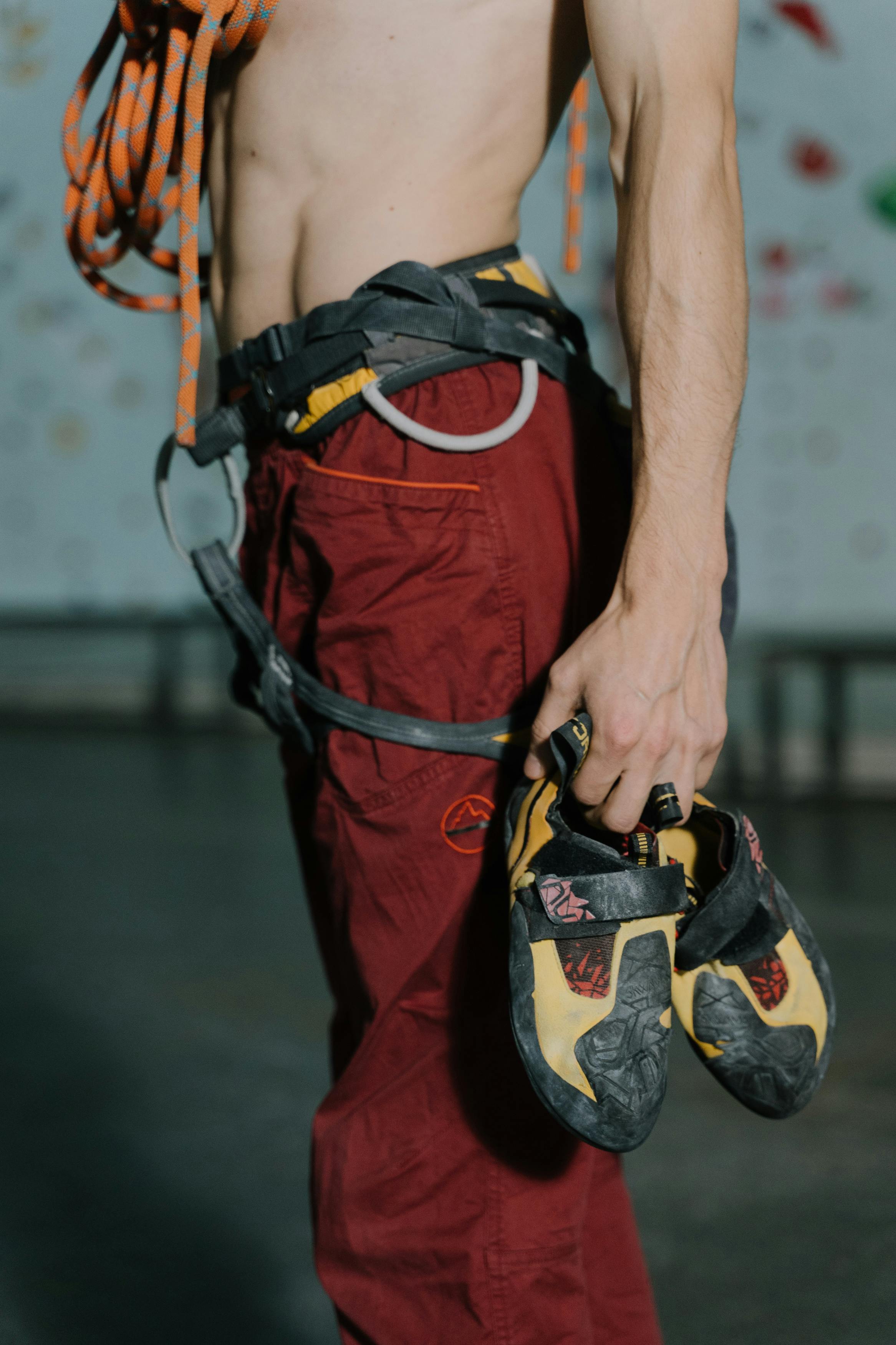 Close-up of a climber holding shoes in an indoor gym setting. Focus on sports gear.