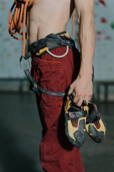 Close-up of a climber holding shoes in an indoor gym setting. Focus on sports gear.