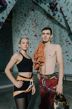 Two rock climbers pose confidently in a modern indoor climbing gym.