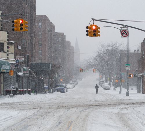 Free A snow-covered urban street with traffic lights and a lone pedestrian, capturing the essence of winter in the city. Stock Photo
