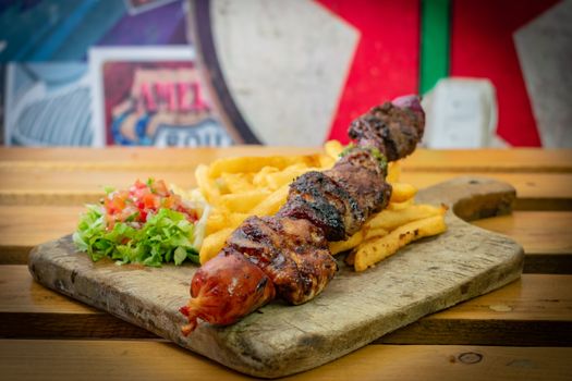 Delicious grilled skewer served with fries and salad on a rustic board. Perfect fast food meal.