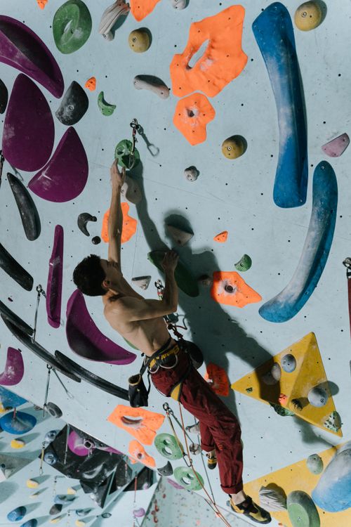 Free Adult male climber scaling a colorful indoor climbing wall, focusing on fitness and sport. Stock Photo