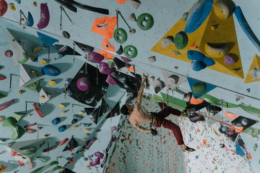 Shirtless climber tackling a challenging indoor rock climbing wall, showcasing vibrant holds and dynamic movement.