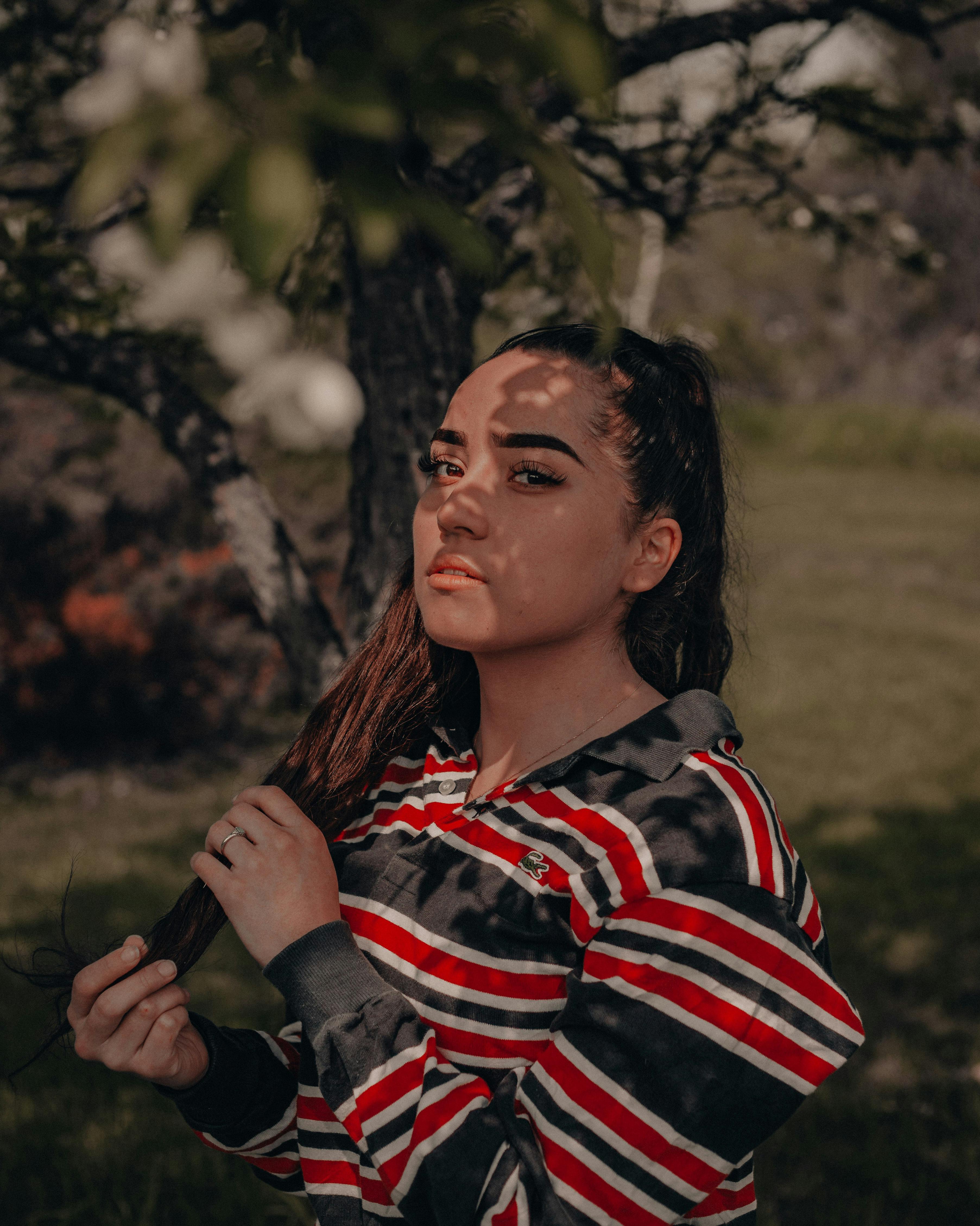 A woman poses outdoors with shadows on her face, wearing a striped shirt. Captured in Ontario, Canada.