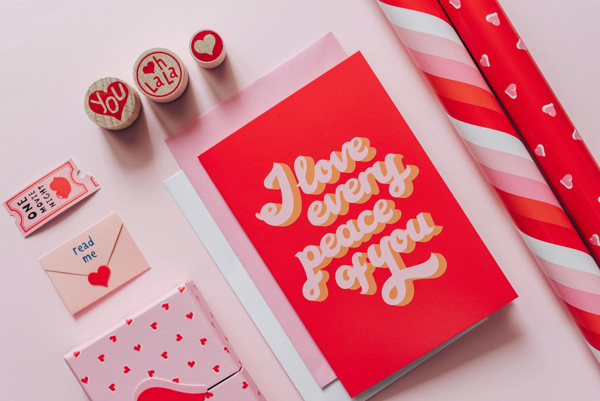 Flat lay of romantic cards and gift wraps with love messages on a pink background.