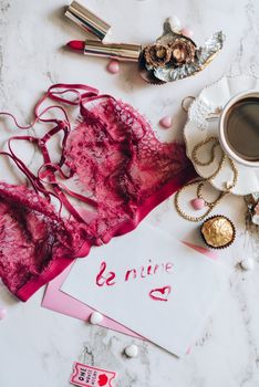 A romantic flat lay with pink lingerie, chocolates, coffee, and a 'be mine' card.