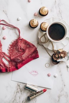 Stylish flat lay of coffee, lipstick, lingerie, and chocolates on marble.