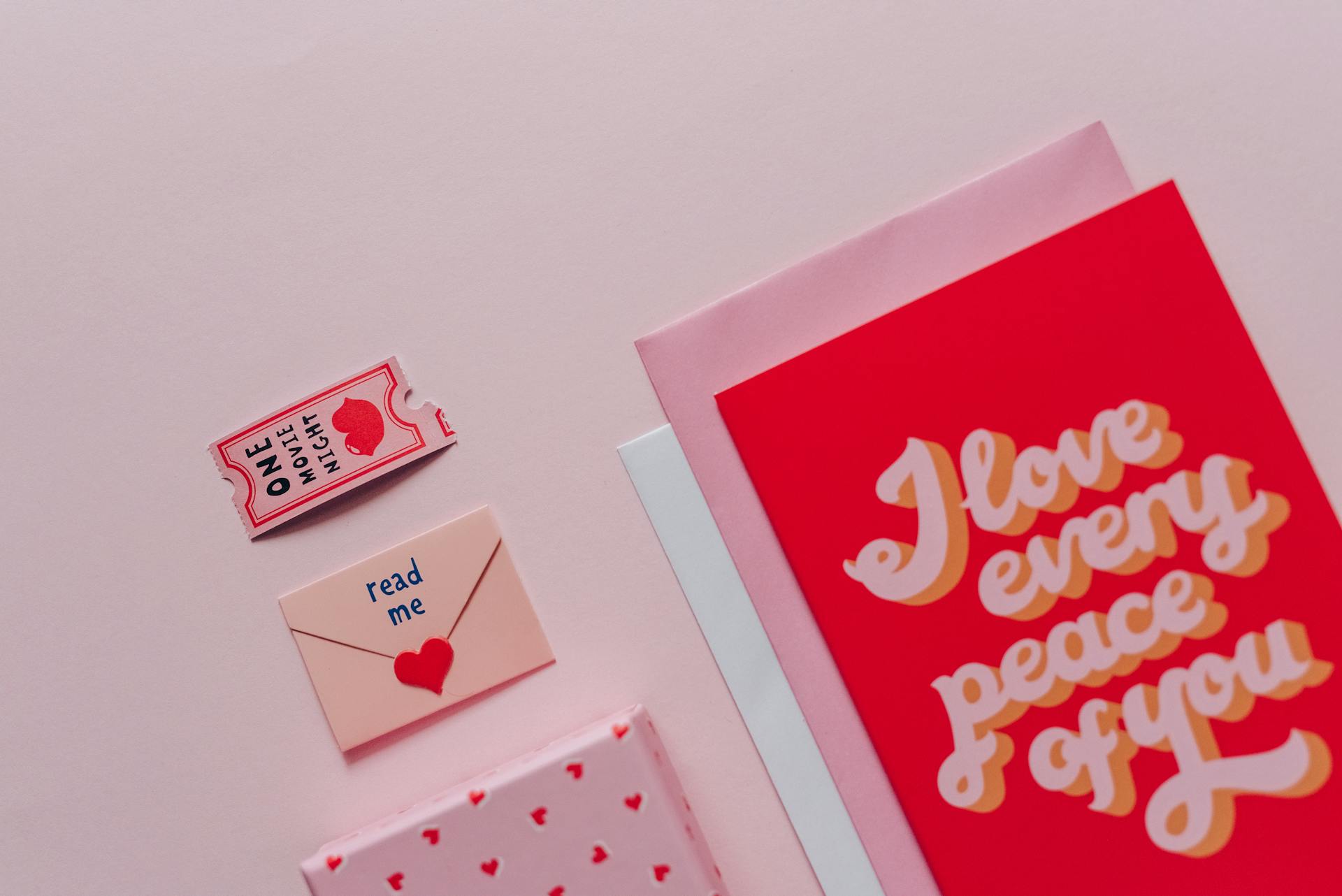 Flat lay of romantic cards and envelopes with love messages on a soft pink background.