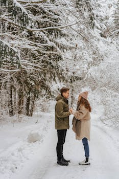 A couple enjoys a romantic moment in a snowy forest holding hands, surrounded by winter trees.