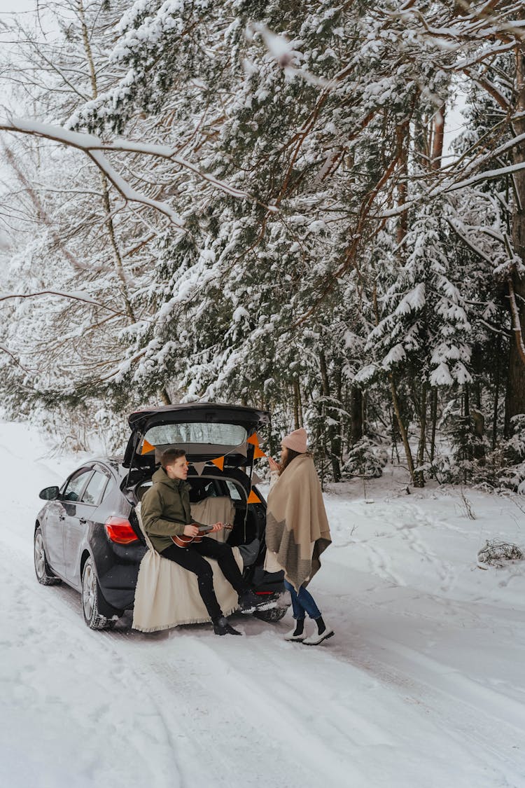 A Man Sitting At The Trunk Of The Car While Talking To The Woman Wearing A Scarf