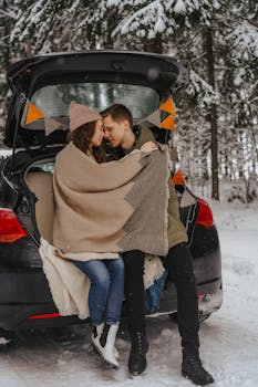 Couple wrapped in blankets enjoying a winter day in the car trunk amidst snow.