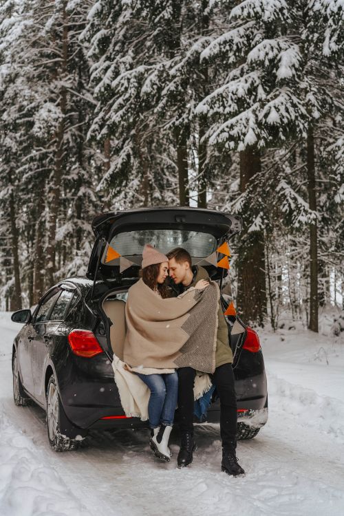 Free A couple wrapped in blankets embrace in the trunk of a car amidst a snowy forest landscape. Stock Photo