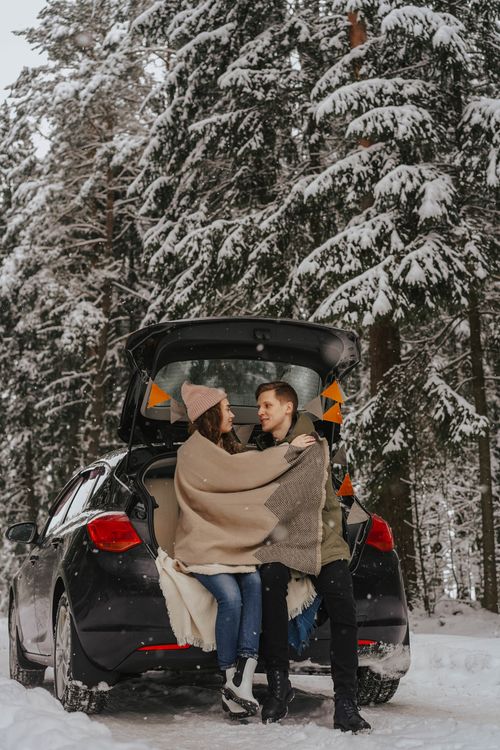 Free A couple enjoys a warm embrace in a snowy forest, sitting at the back of a car. Stock Photo