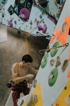 Shirtless man climbs colorful indoor rock wall, showcasing strength and agility.