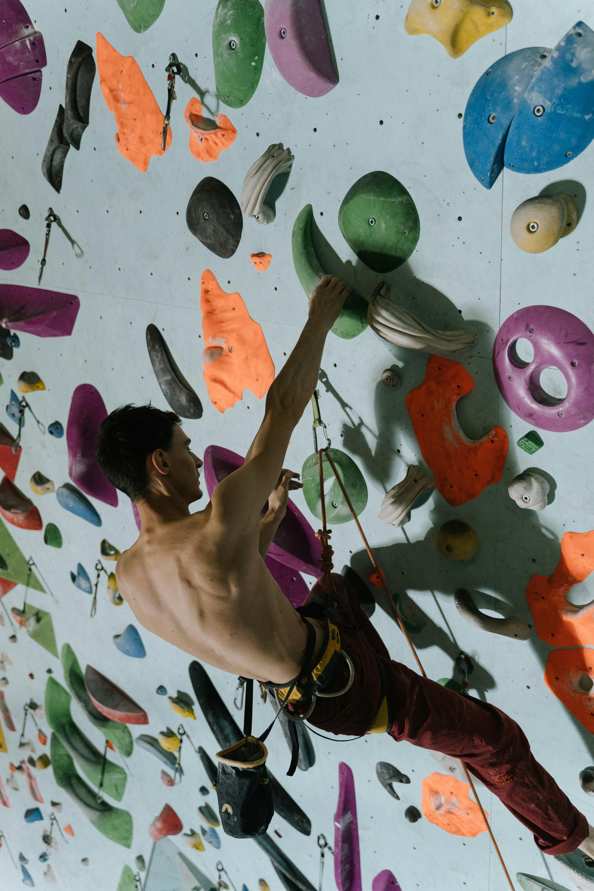 Athletic man climbing a vibrant, multi-colored indoor bouldering wall, showcasing fitness and strength.