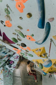 Adult man rock climbing indoors on a vibrant bouldering wall. Sport and adventure concept.