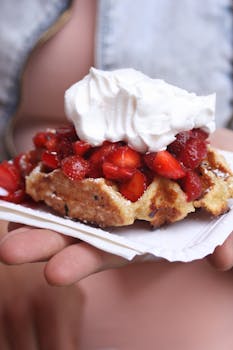 Close-up of a strawberry-topped waffle with whipped cream held outdoors.