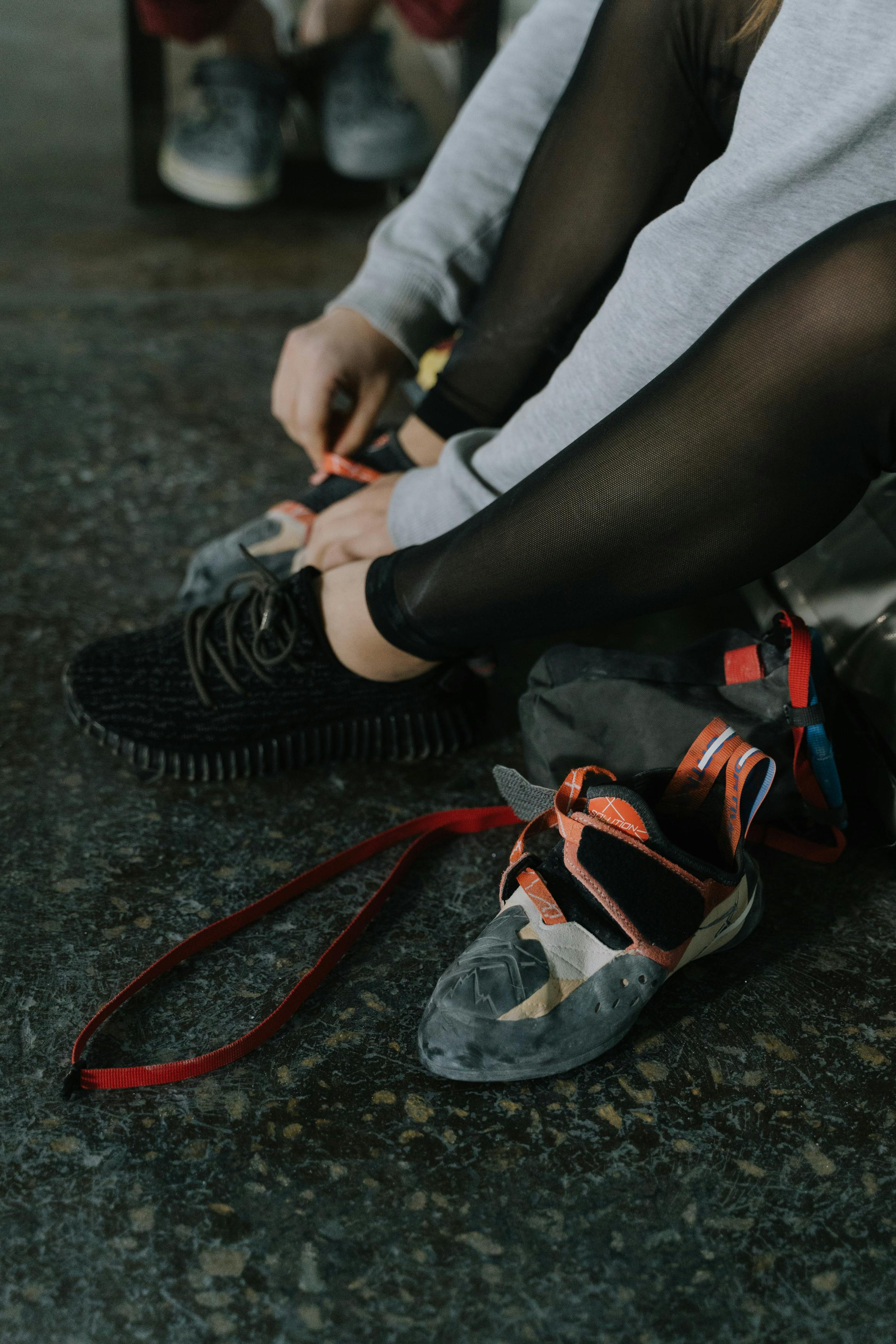 Close-up of a woman preparing for climbing, tying climbing shoes indoors.