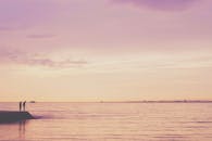 在宁静的海洋日落中，两个人物的剪影映衬出紫色的色调和遥远的城市天际线