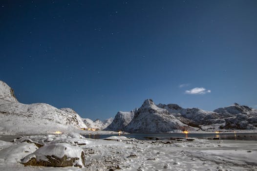Beautiful snowy mountain landscape under a starry night sky with gentle illumination from a nearby village.