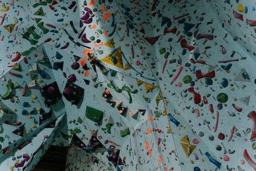 Indoor climbing wall with colorful holds and a climber ascending, showcasing a dynamic sport environment.
