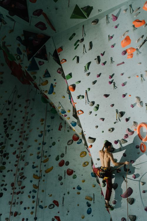 Free A man skillfully climbs an indoor rock wall with colorful climbing holds. Stock Photo