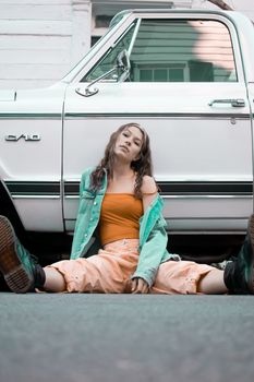 Fashion-forward woman sitting in casual attire before a vintage car, exuding confidence.