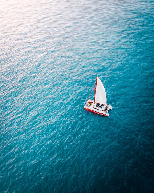 Drone view of modern vessel with white sails floating in turquoise water of rippling sea in nature on summer day