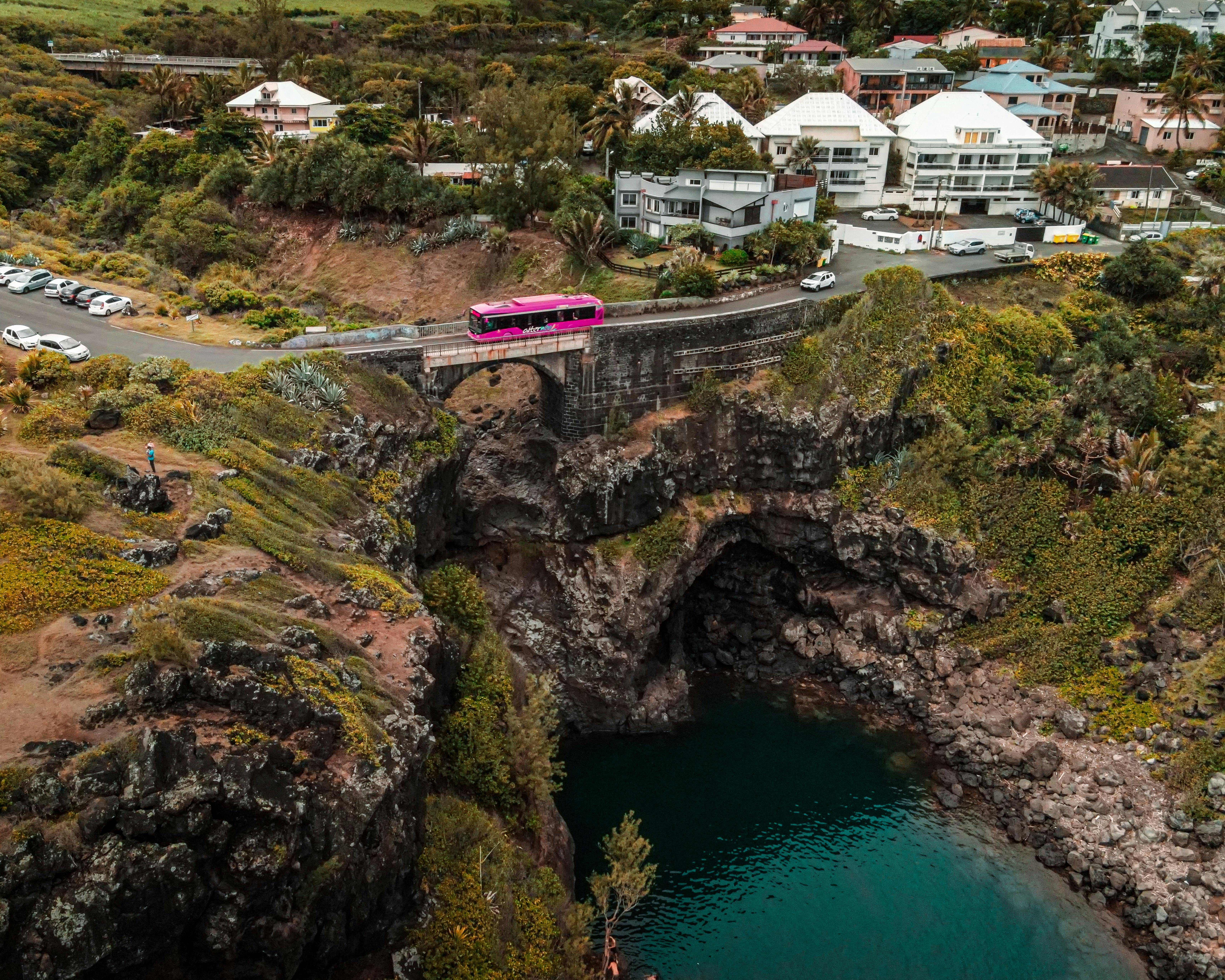 Bridge above turquoise water located in mountainous area covered with grass in small town with residential buildings among green trees