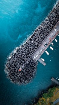 Drone view of lighthouse near parked cars and moored yachts located on harbor near calm azure sea in coastal area