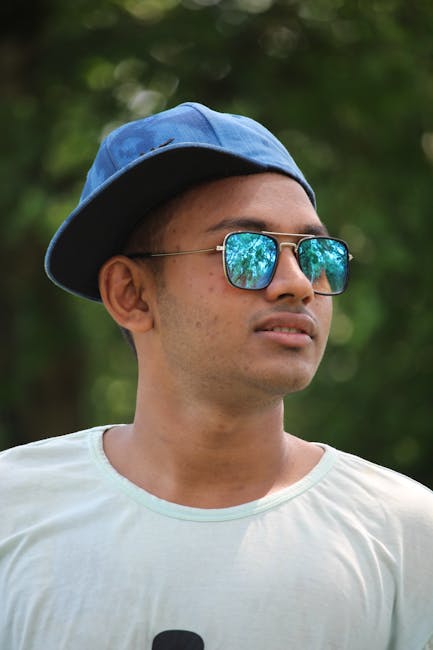 Portrait of a young man wearing sunglasses and a cap, set against a natural outdoor background.
