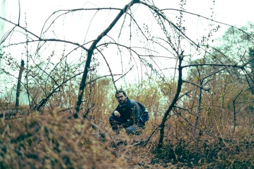 Free A man crouches among dry, leafless bushes during an autumn exploration adventure. Stock Photo