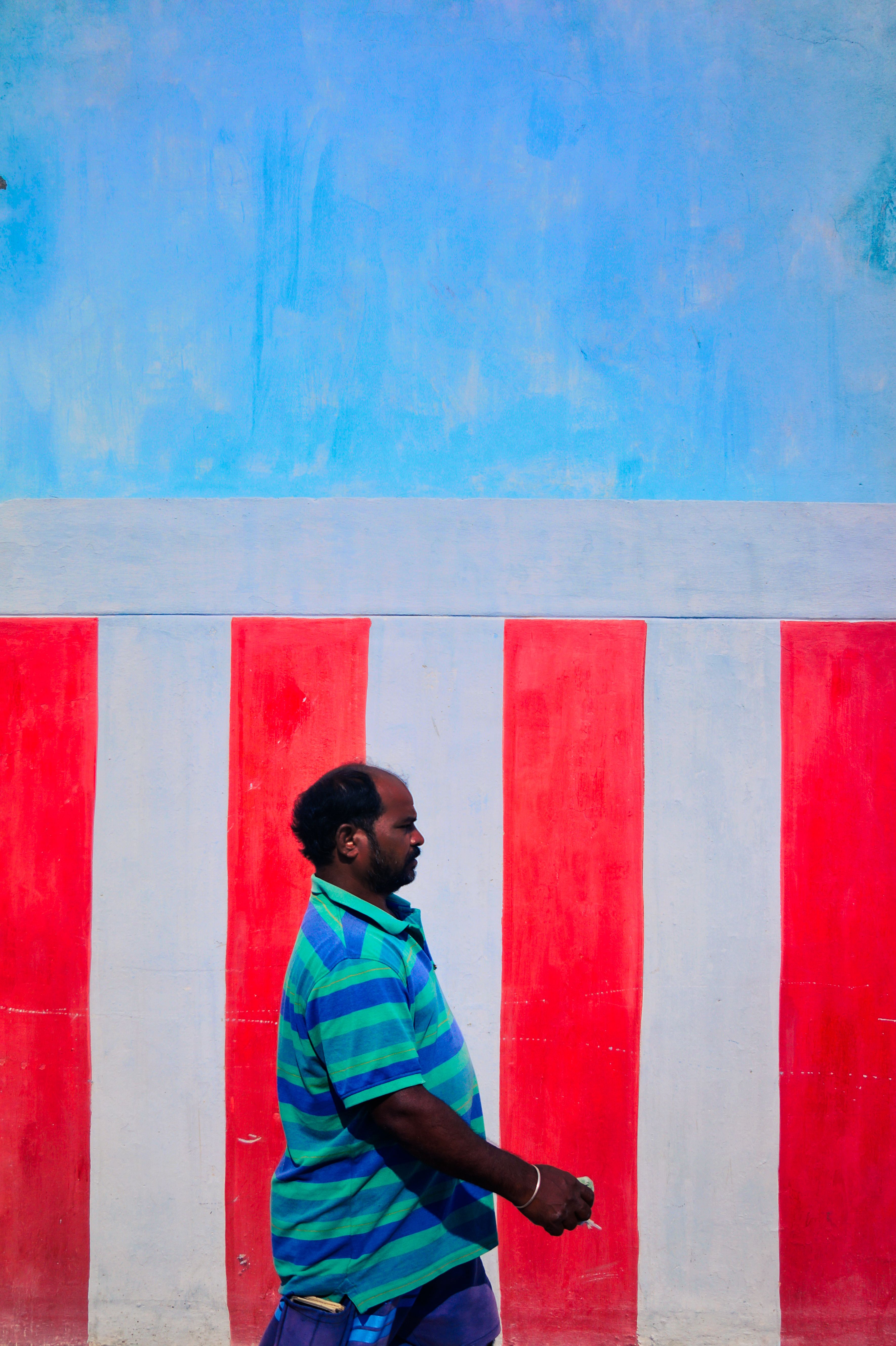 Profile view of a man walking past a striking blue and red striped wall.