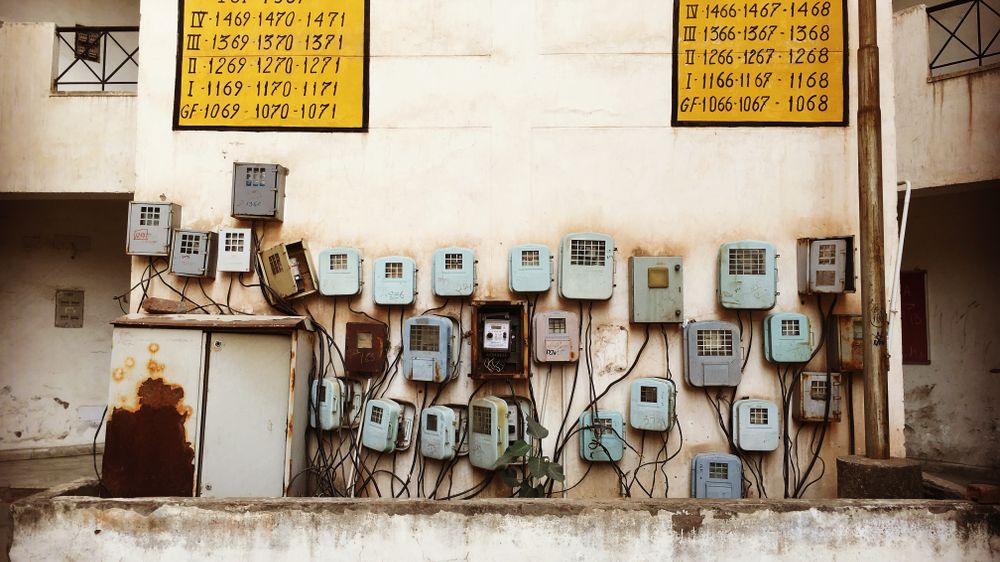 Aged electrical meters and wiring mounted on a concrete wall of an old building in India.