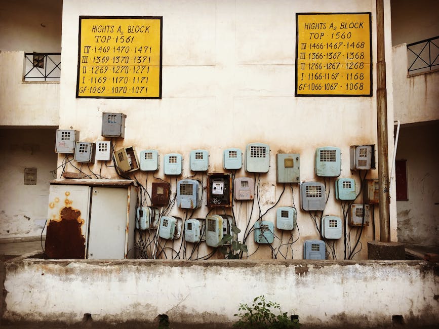 Aged electrical meters and wiring mounted on a concrete wall of an old building in India.