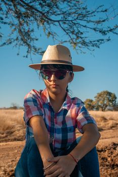 Portrait of a young woman wearing a cowboy hat and sunglasses, enjoying a sunny day outdoors.