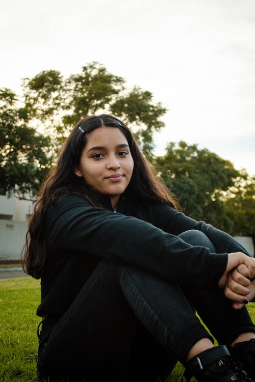 Free A teenager sitting on grass in a park, looking thoughtful and relaxed. Stock Photo