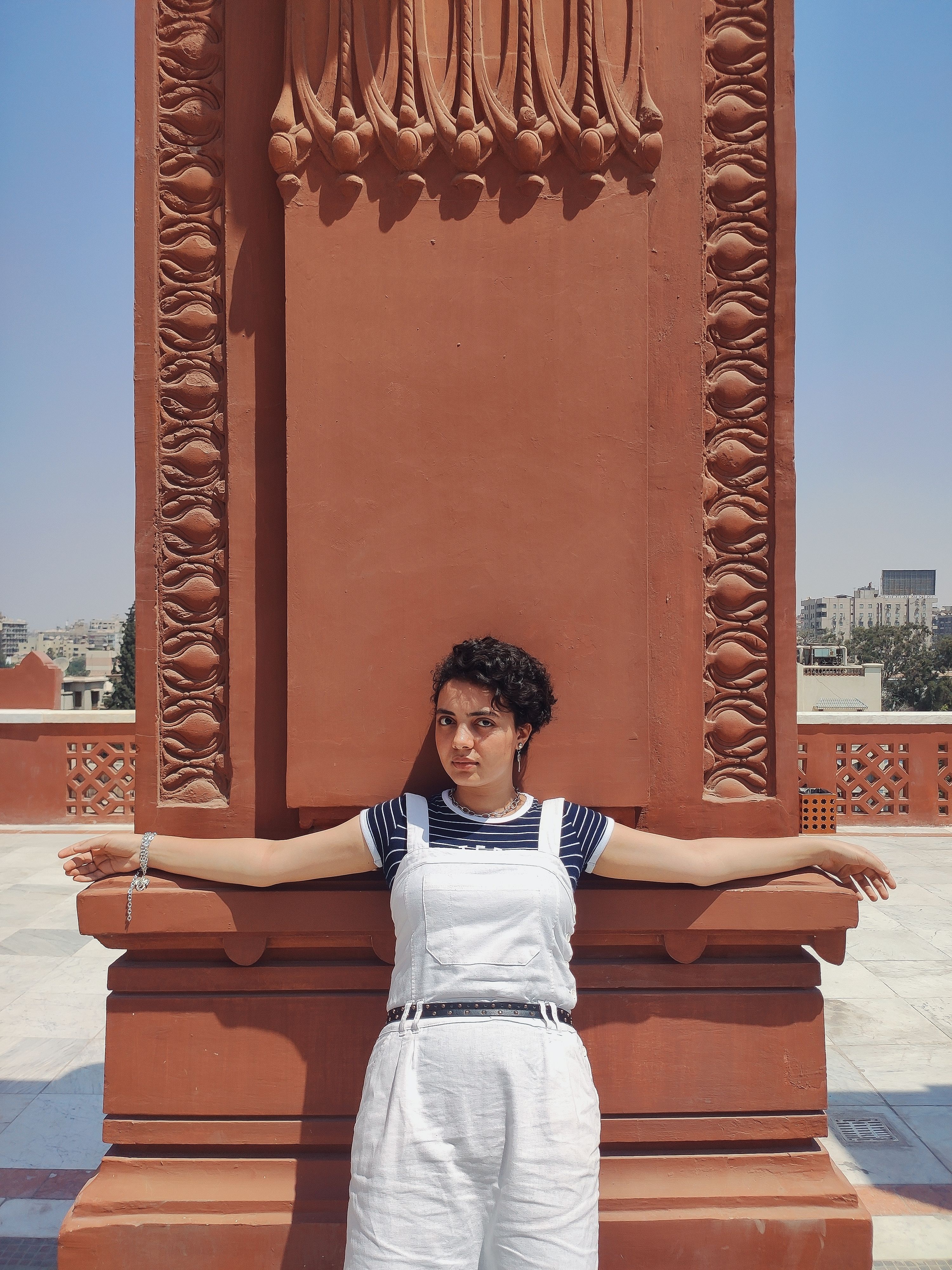 Urban portrait of a woman leaning against a decorative monument on a sunny day.