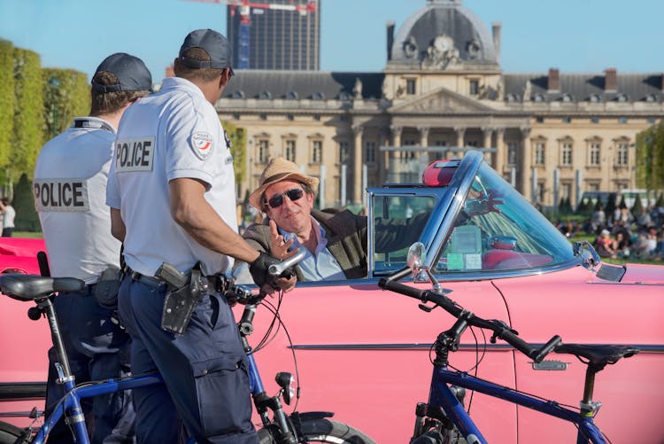 Man Talking To A Police Officers While Sitting In A Pink Vintage Car