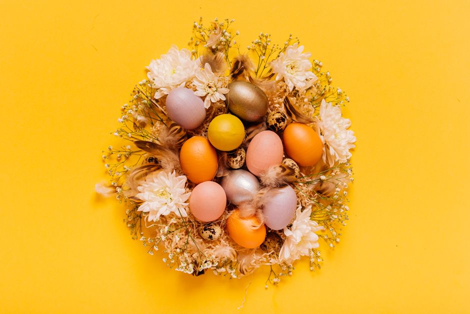 Vibrant Easter eggs nestled in flowers on a bright yellow background.