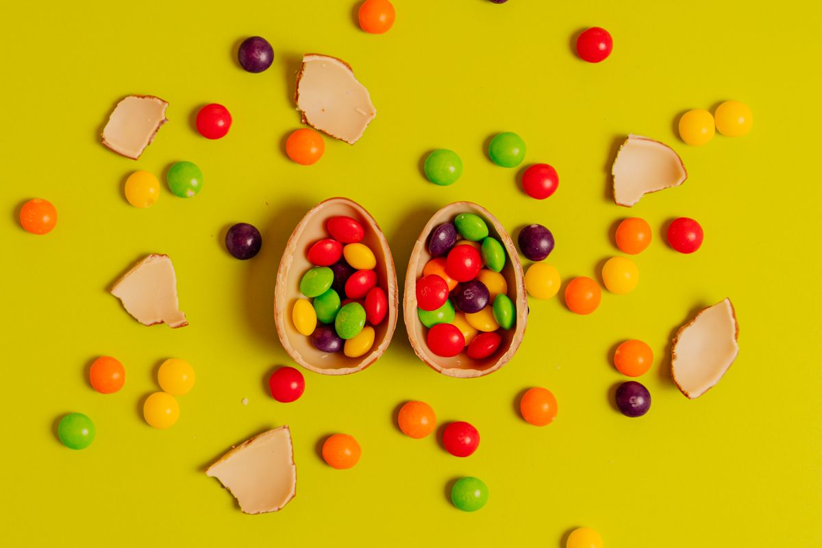 Vibrant candies spilling from a chocolate eggshell against a yellow background.