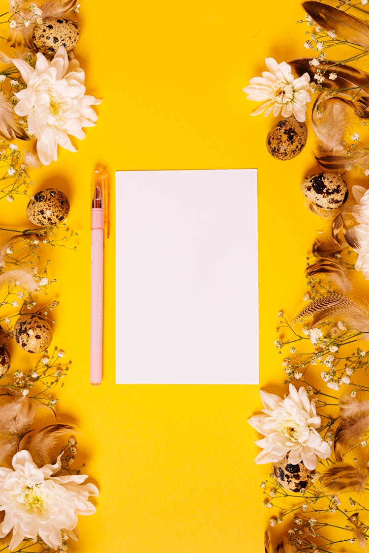 A Blank Paper Surrounded With Flowers And Feathers On A Yellow Background