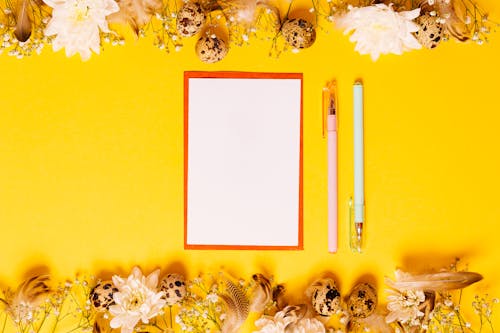 
A Blank Paper beside Pens on a Yellow Surface
