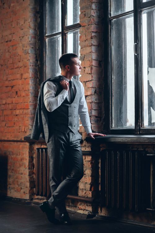 Free Elegant man in formal attire standing and looking through a loft window with exposed bricks. Stock Photo