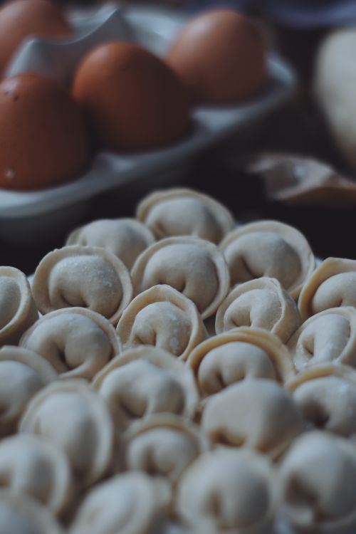Free Detailed view of uncooked pelmeni on a kitchen surface with eggs in the background. Stock Photo