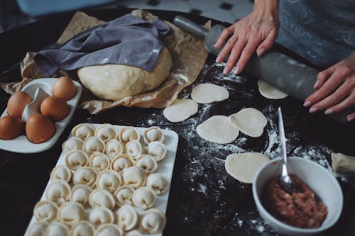 A person Using a Rolling Pin on a Piece of Dumpling Dough