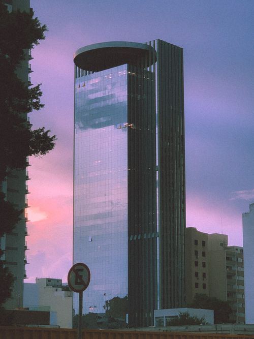 Free A modern glass skyscraper stands tall against a vibrant purple and pink sunset sky, reflecting urban architecture. Stock Photo
