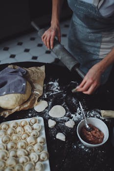 Close-up of hands preparing traditional Russian pelmeni dumplings from scratch on a kitchen table.