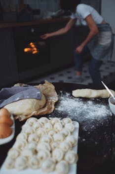 A woman bakes dumplings in the kitchen, with dough and ingredients on the counter.