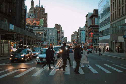 Free Group of people walking on pedestrian crossing on asphalt road with cars in city with residential buildings in evening time Stock Photo